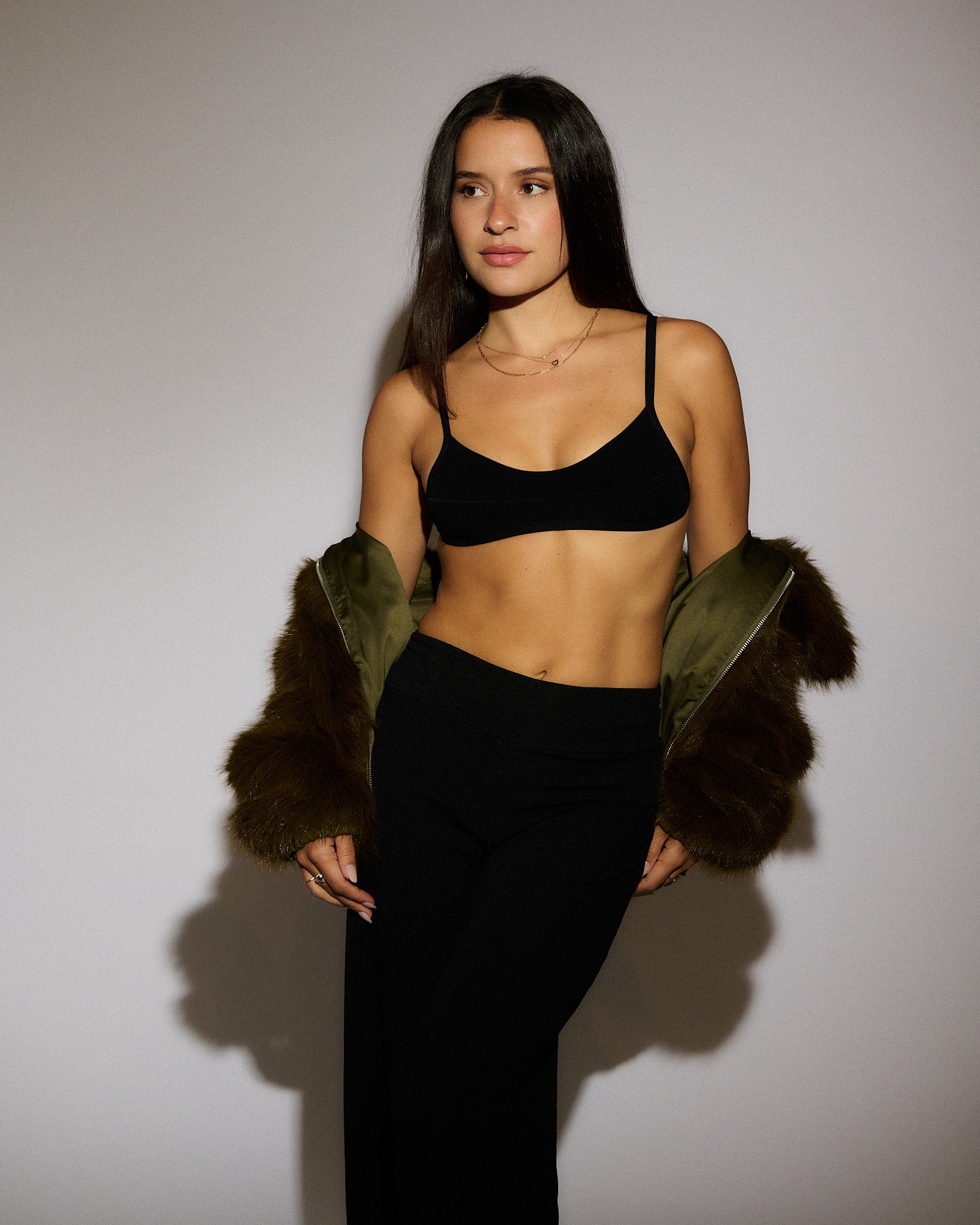 Woman standing on a gray background wearing a black Scoop Nuudii, black pants, and a green fuzzy jacket.