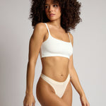 Woman wearing a white cropped cami on a plain background