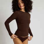 Woman wearing a brown long-sleeve bodysuit against a plain background