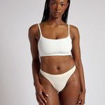 Woman wearing a white cropped cami on a plain background