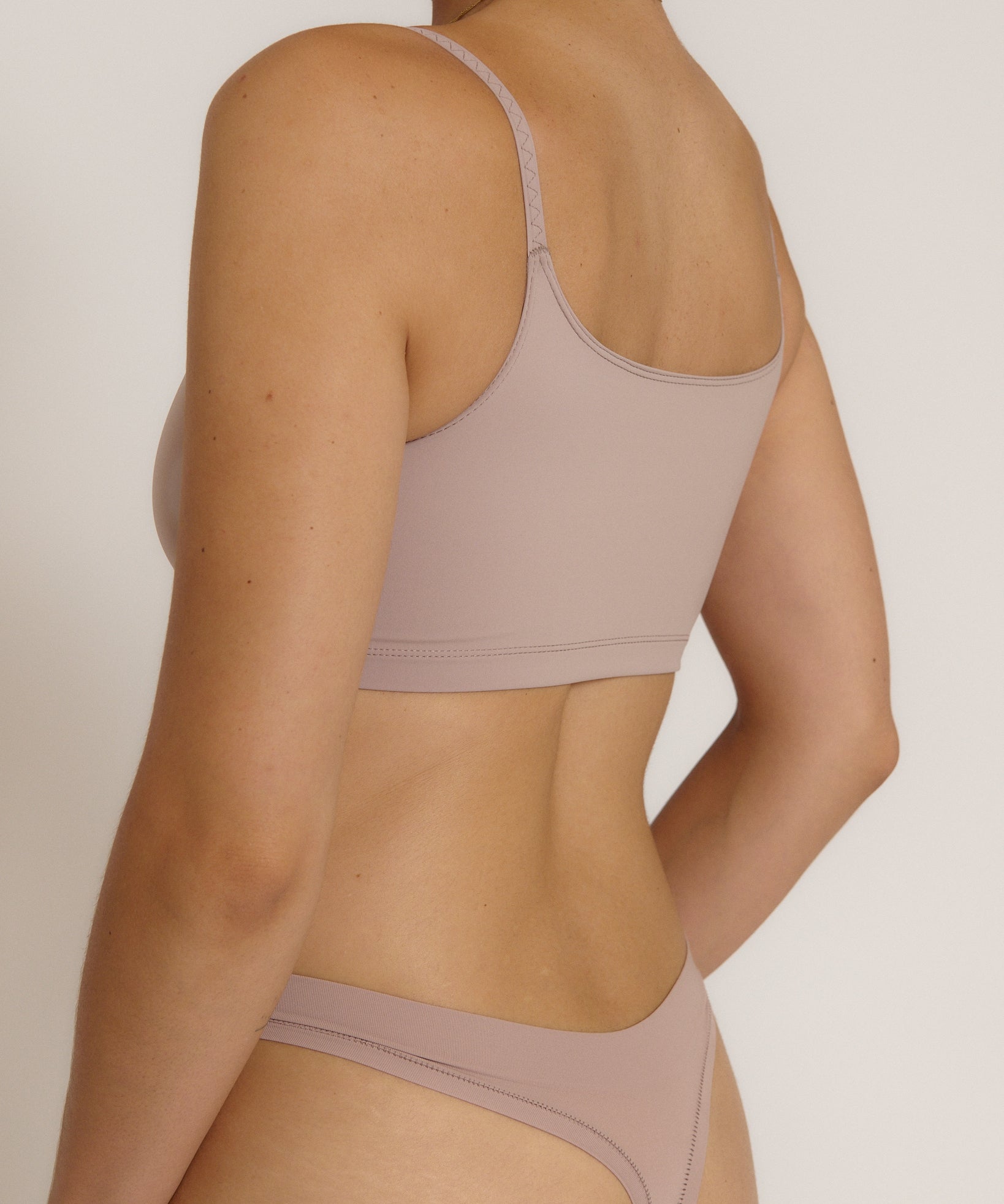 A woman modeling a dusk cropped cami and matching underwear, against a plain light beige studio background.