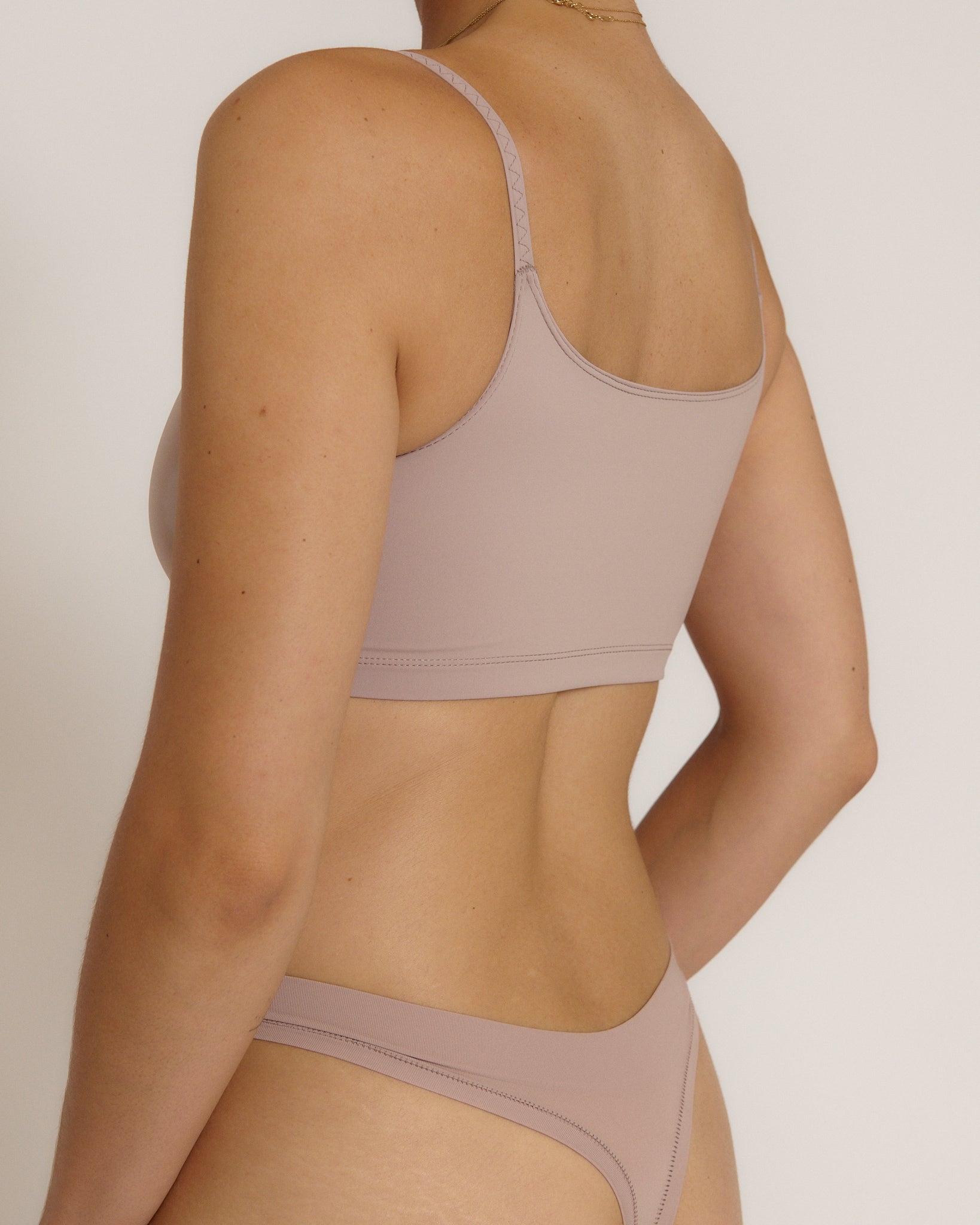 A woman modeling a dusk cropped cami and matching underwear, against a plain light beige studio background.