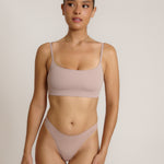 A woman modeling a dusk cropped cami and matching underwear, against a plain light beige studio background.