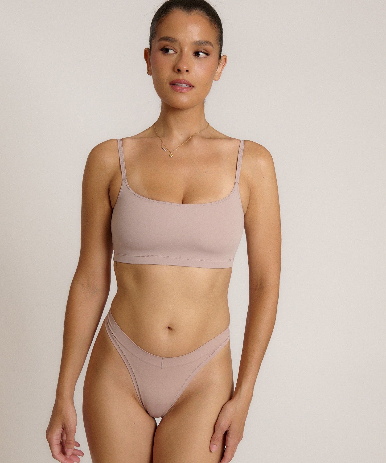 A woman modeling a dusk cropped cami and matching underwear, against a plain light beige studio background.
