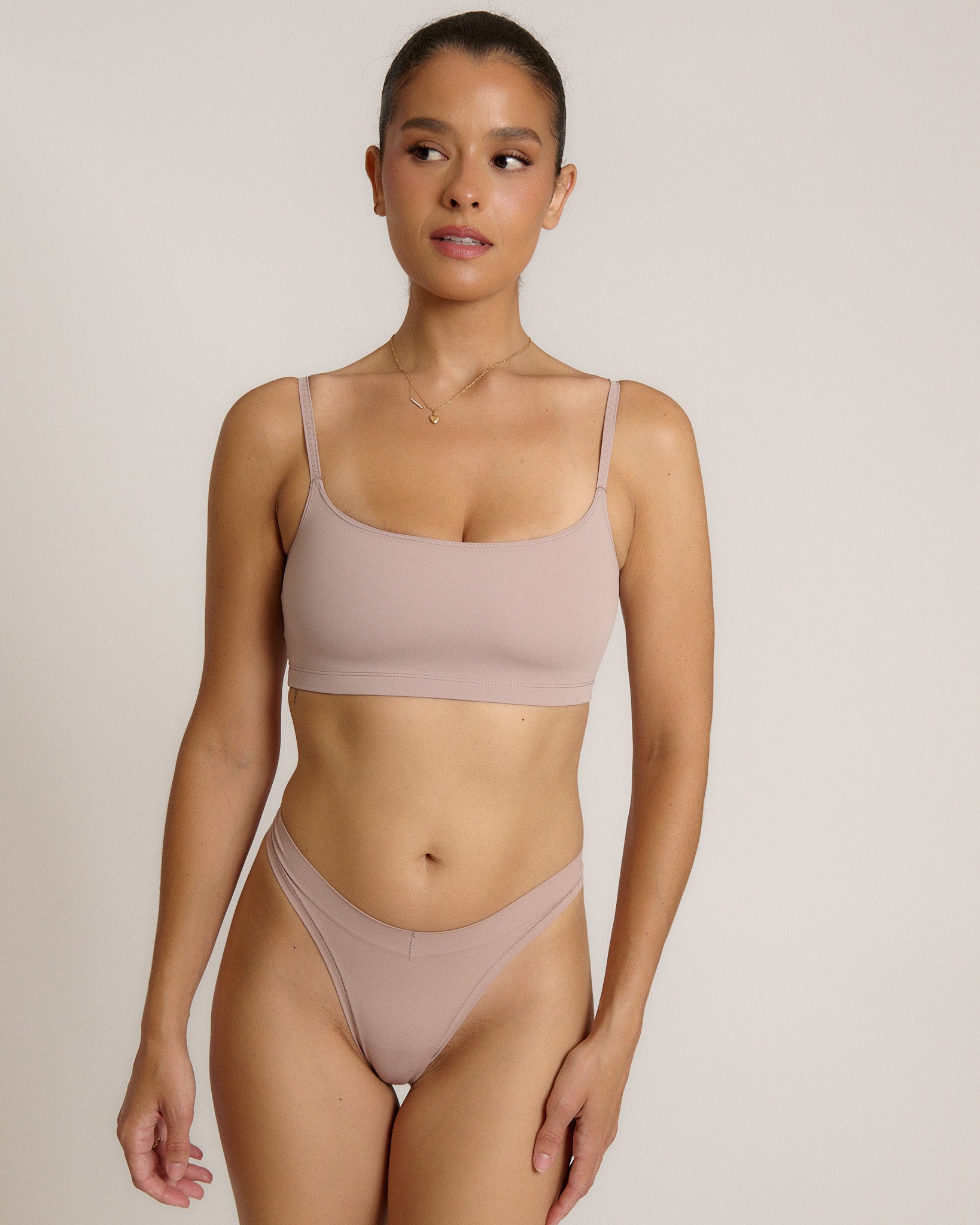 A woman modeling a dusk cropped cami and matching underwear, against a plain light beige studio background.