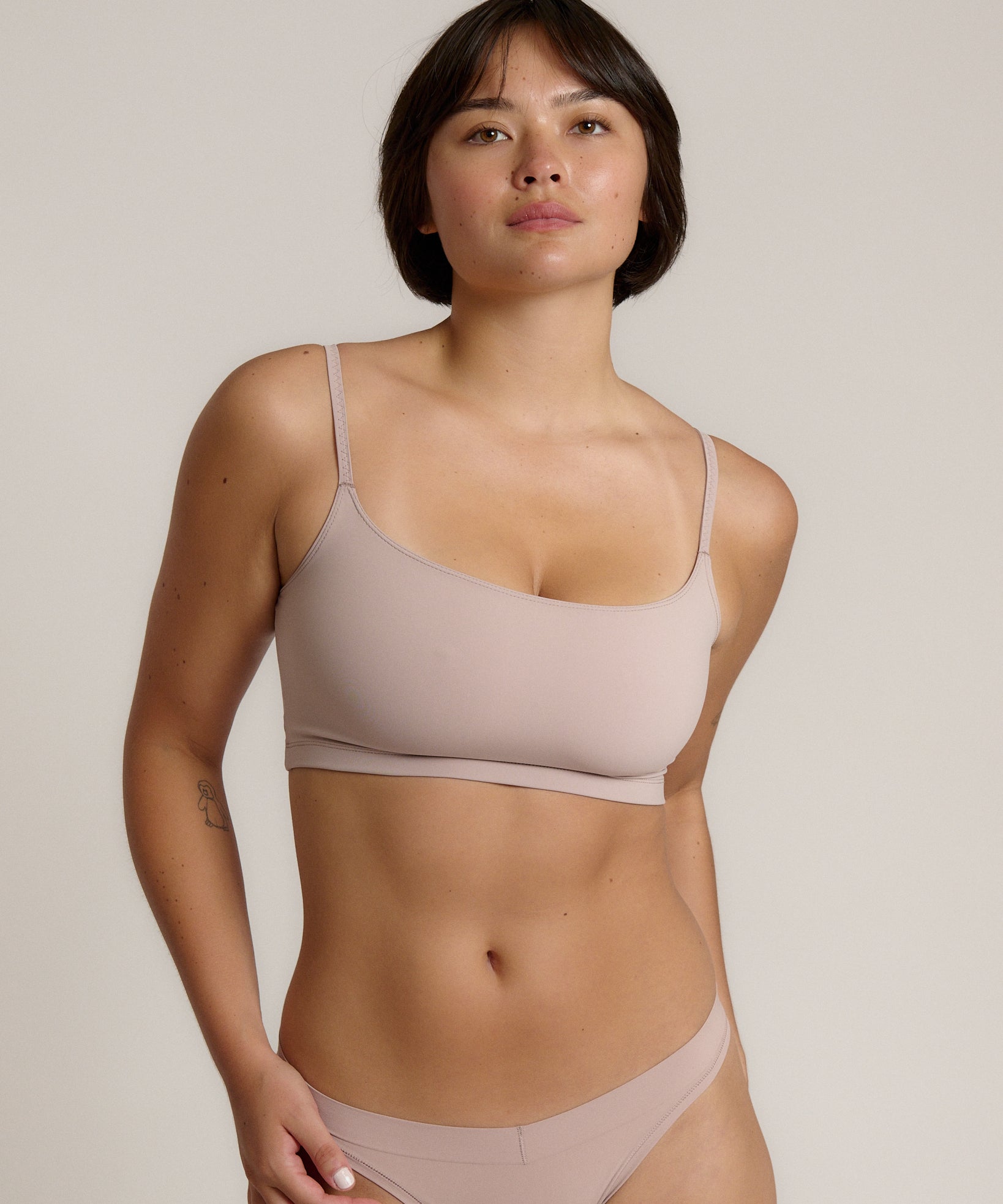 A woman modeling a dusk cropped cami and matching underwear, against a plain light beige studio background.