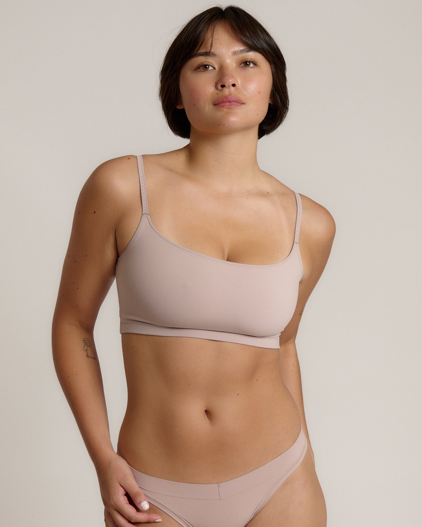 A woman modeling a dusk cropped cami and matching underwear, against a plain light beige studio background.