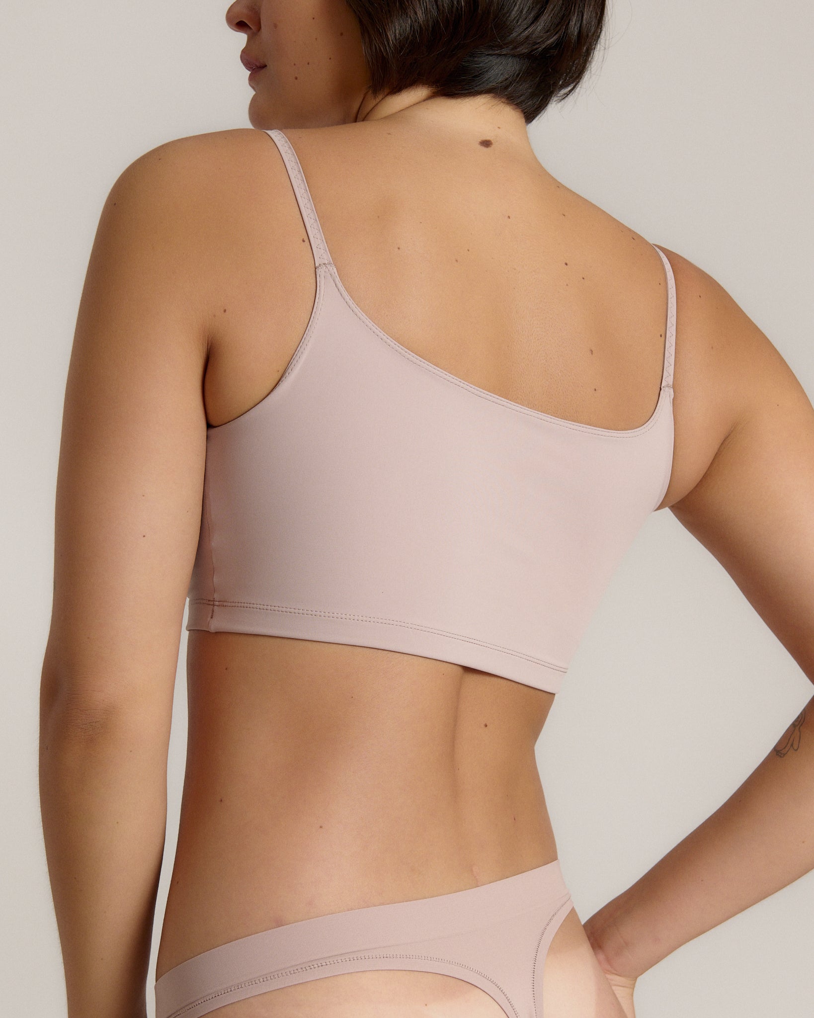A woman modeling a dusk cropped cami and matching underwear, against a plain light beige studio background.