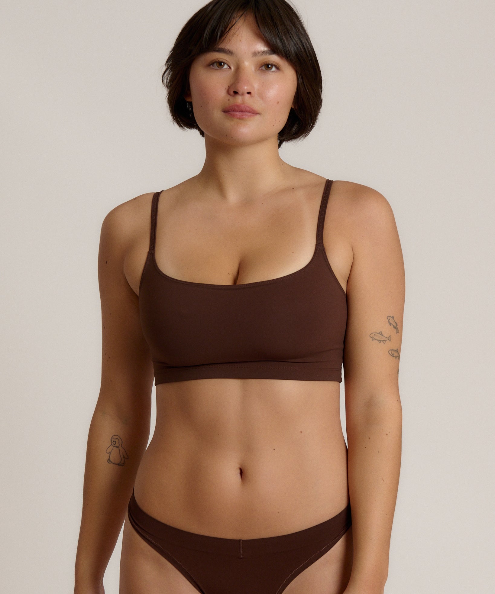 A woman modeling a matching mocha cropped cami and underwear set against a plain light beige studio background.