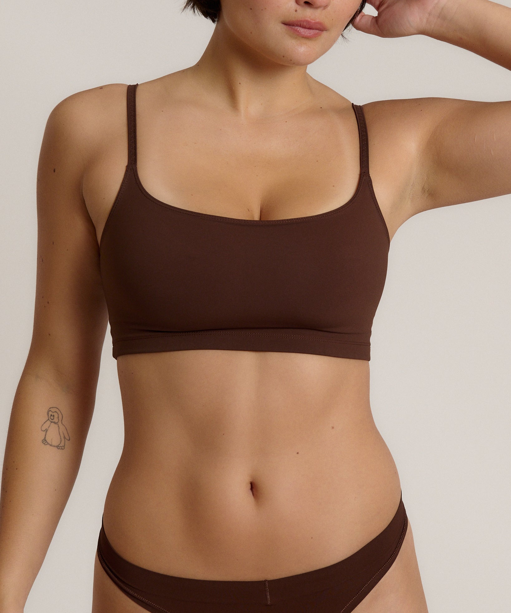 A woman modeling a matching mocha cropped cami and underwear set against a plain light beige studio background.