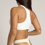 Woman wearing a white racerback on a plain background