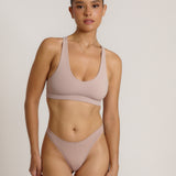 A woman modeling a dusk cropped racerback and matching underwear, against a plain light beige studio background.