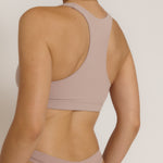 A woman modeling a dusk cropped racerback and matching underwear, against a plain light beige studio background.