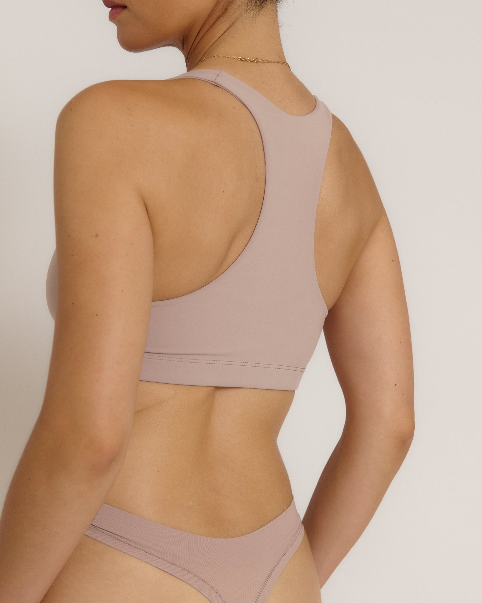 A woman modeling a dusk cropped racerback and matching underwear, against a plain light beige studio background.