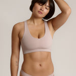 A woman modeling a dusk cropped racerback and matching underwear, against a plain light beige studio background.