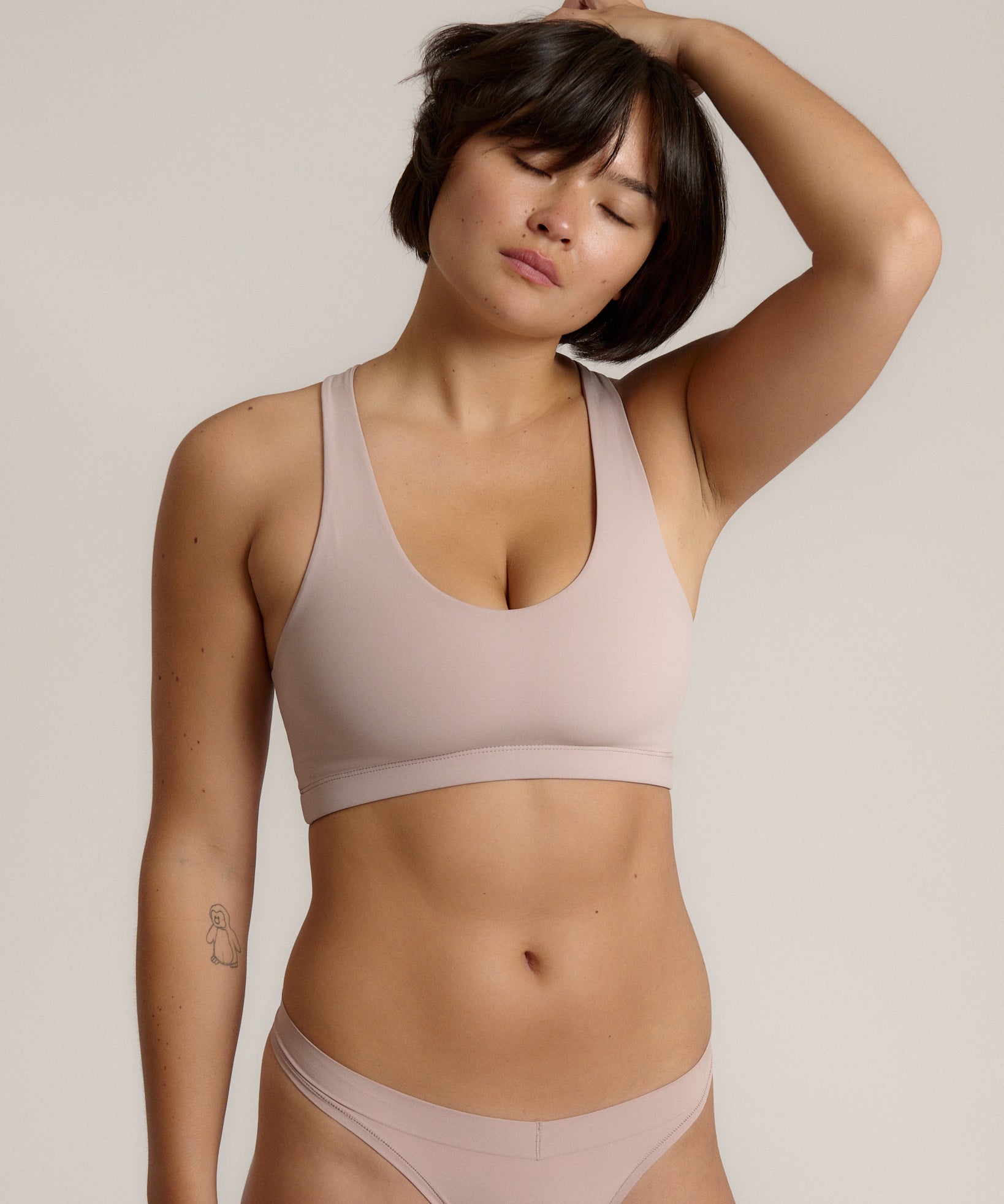 A woman modeling a dusk cropped racerback and matching underwear, against a plain light beige studio background.