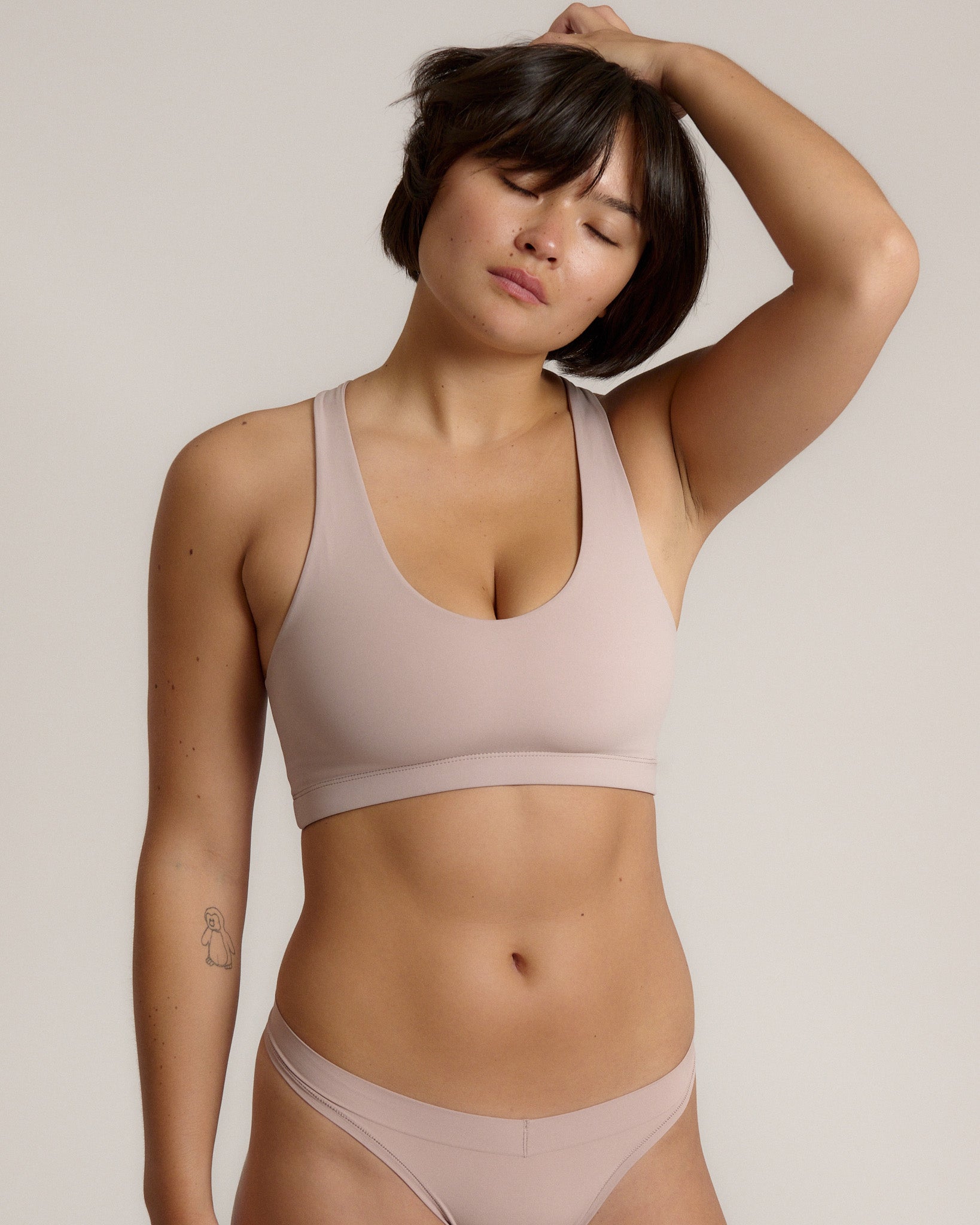 A woman modeling a dusk cropped racerback and matching underwear, against a plain light beige studio background.