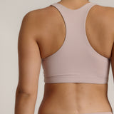 A woman modeling a dusk cropped racerback and matching underwear, against a plain light beige studio background.