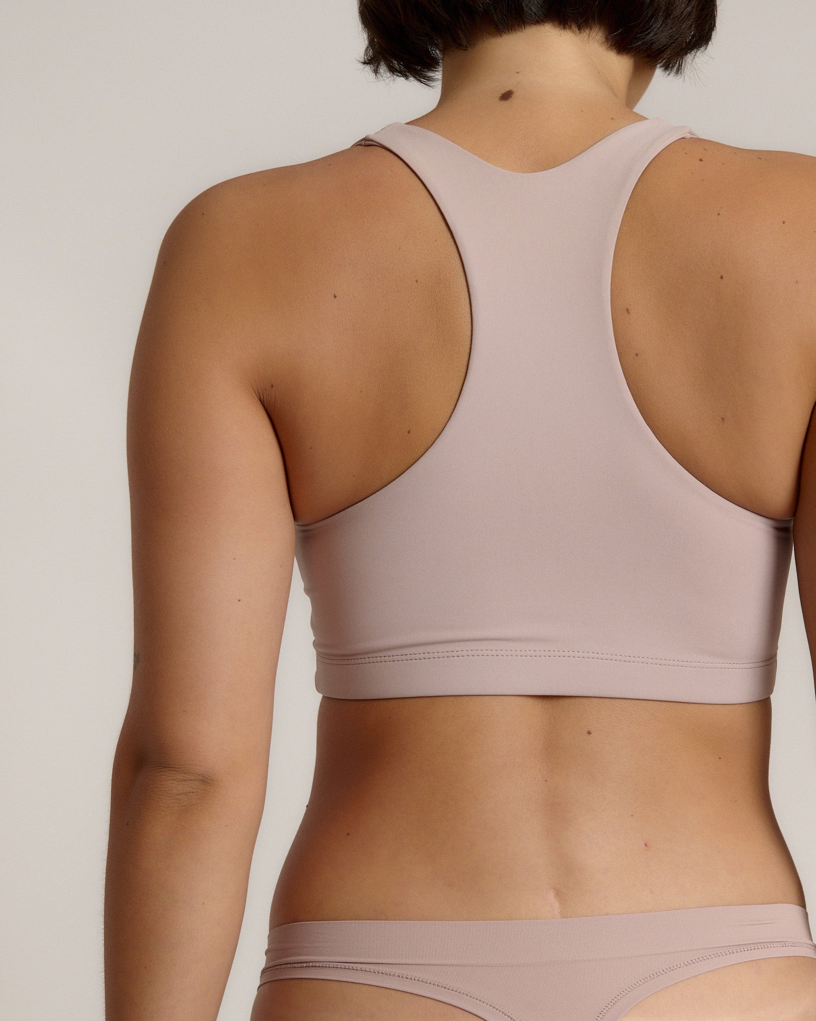 A woman modeling a dusk cropped racerback and matching underwear, against a plain light beige studio background.