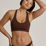 A woman modeling a matching mocha racerback and underwear set against a plain light beige studio background.
