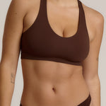 A woman modeling a matching mocha racerback and underwear set against a plain light beige studio background.
