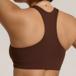 A woman modeling a matching mocha racerback and underwear set against a plain light beige studio background.