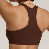 A woman modeling a matching mocha racerback and underwear set against a plain light beige studio background.