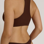 A woman modeling a matching mocha racerback and underwear set against a plain light beige studio background.