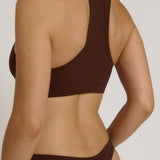 A woman modeling a matching mocha racerback and underwear set against a plain light beige studio background.