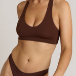 A woman modeling a matching mocha racerback and underwear set against a plain light beige studio background.