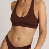 A woman modeling a matching mocha racerback and underwear set against a plain light beige studio background.