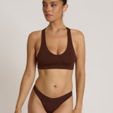 A woman modeling a matching mocha racerback and underwear set against a plain light beige studio background.