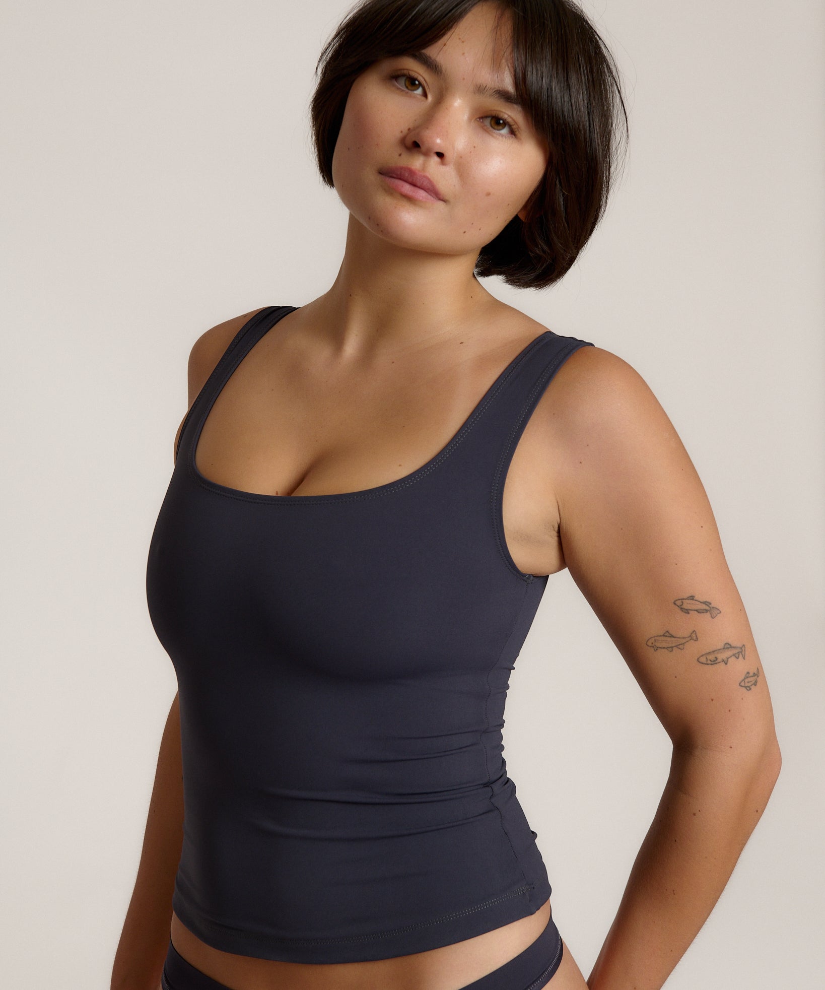 A woman modeling a myst scoop-neck tank top and a matching thong against a plain light gray studio background.