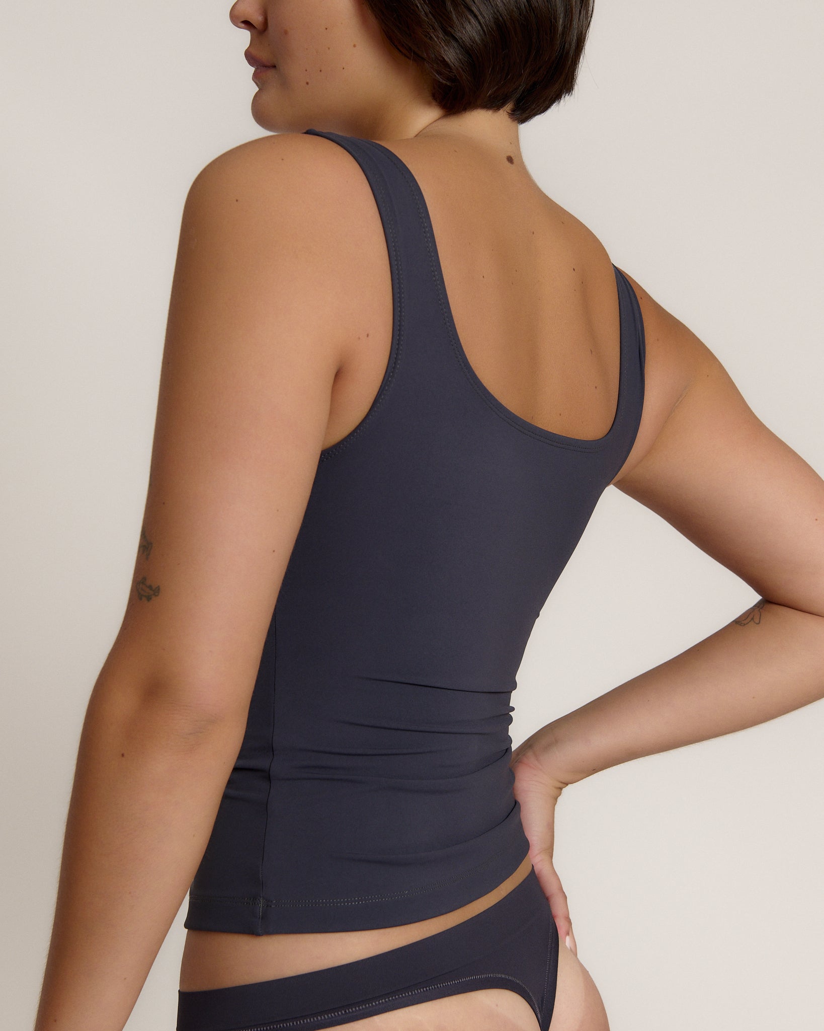 A woman modeling a myst scoop-neck tank top and a matching thong against a plain light gray studio background.