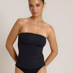 Woman wearing a black strapless top against a gray background