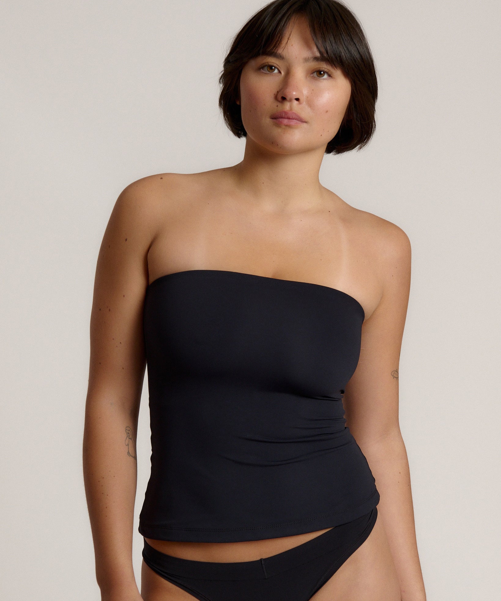 Woman wearing a black strapless top against a gray background