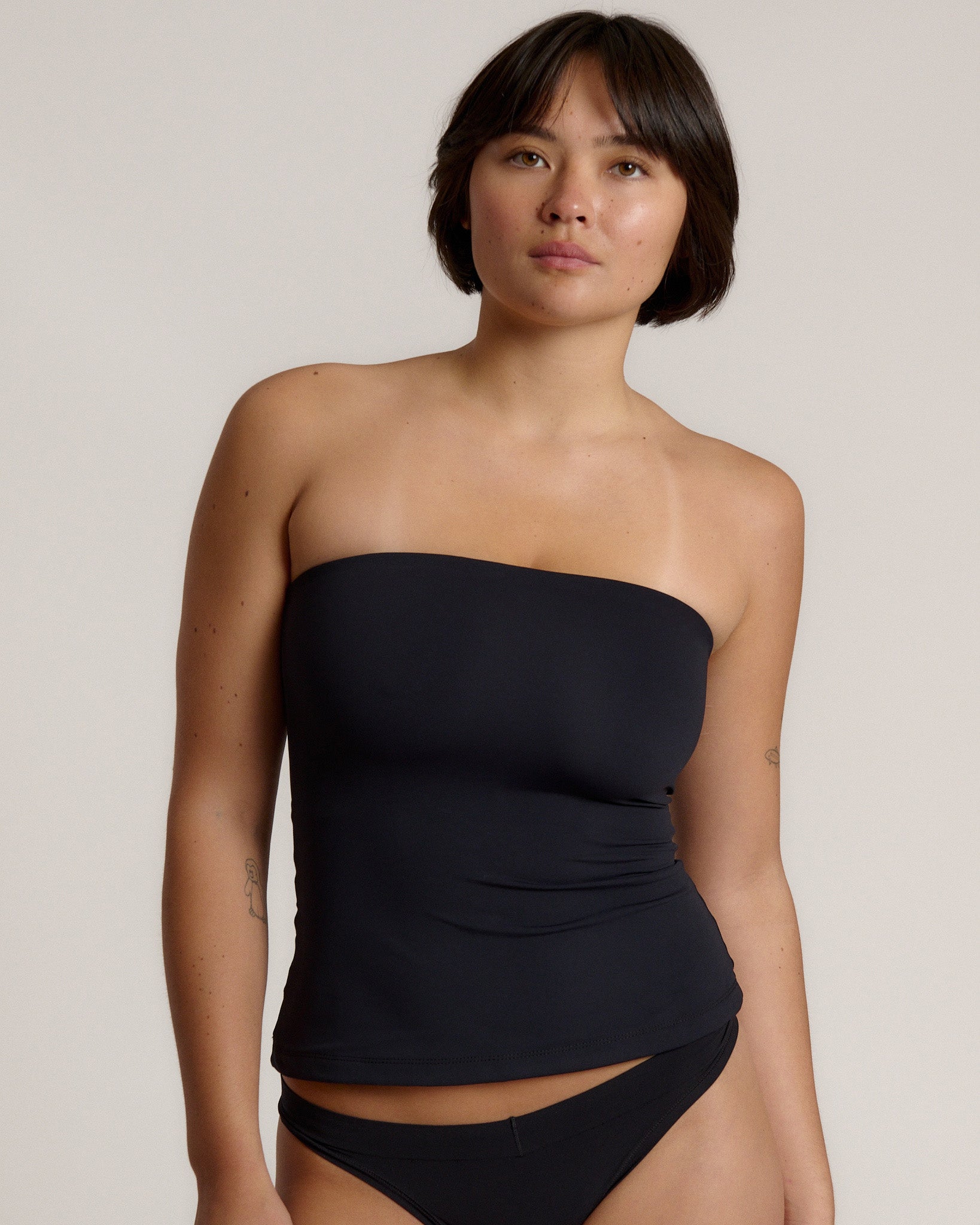 Woman wearing a black strapless top against a gray background