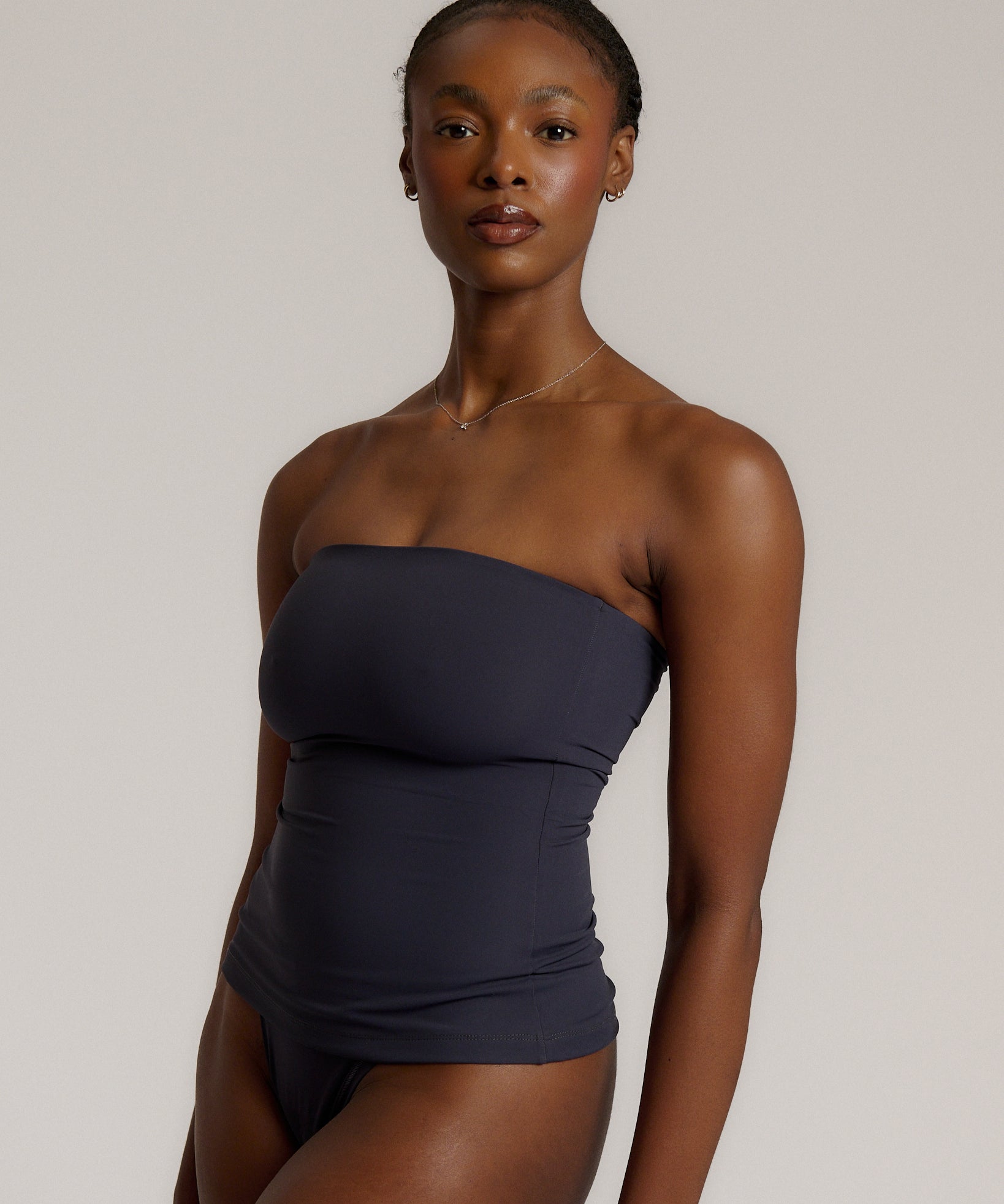A woman modeling a myst tube top and a matching thong against a plain light gray studio background.