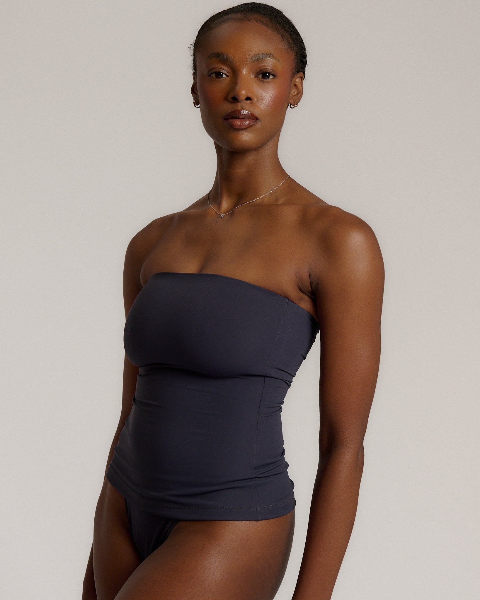 A woman modeling a myst tube top and a matching thong against a plain light gray studio background.