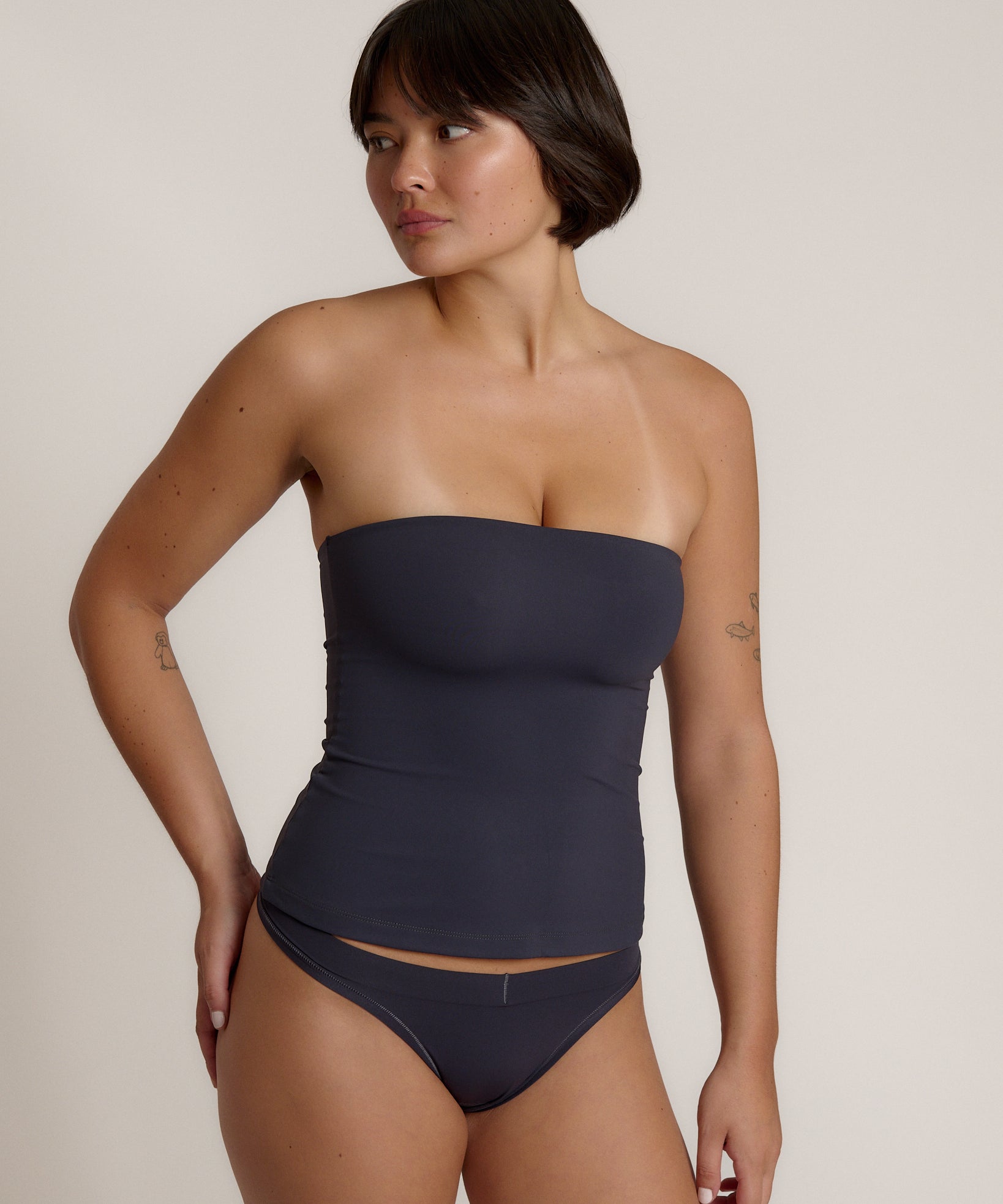 A woman modeling a myst tube top and a matching thong against a plain light gray studio background.