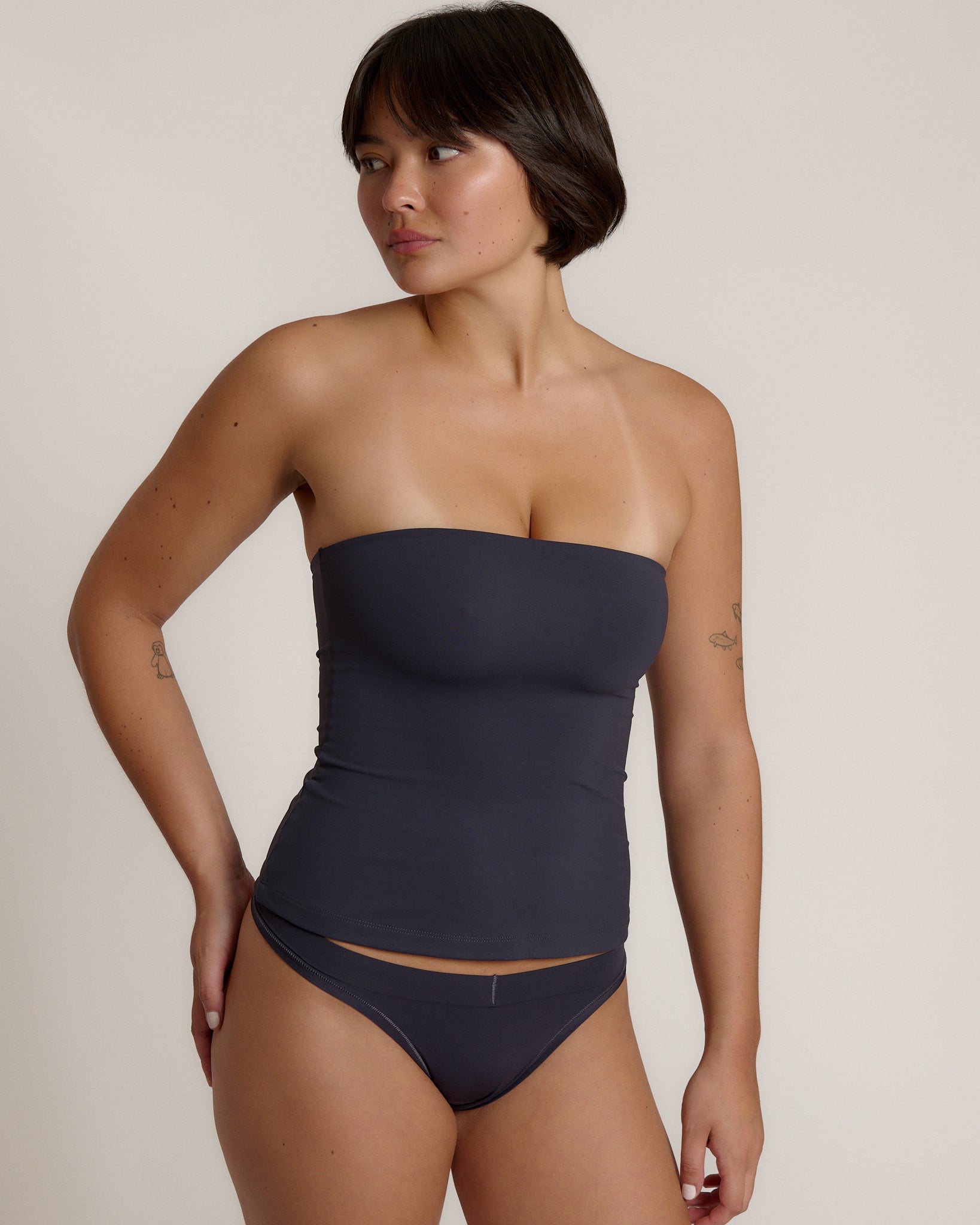 A woman modeling a myst tube top and a matching thong against a plain light gray studio background.