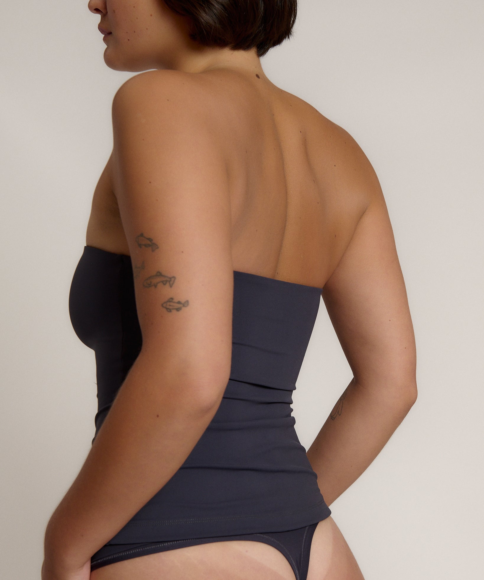 A woman modeling a myst tube top and a matching thong against a plain light gray studio background.