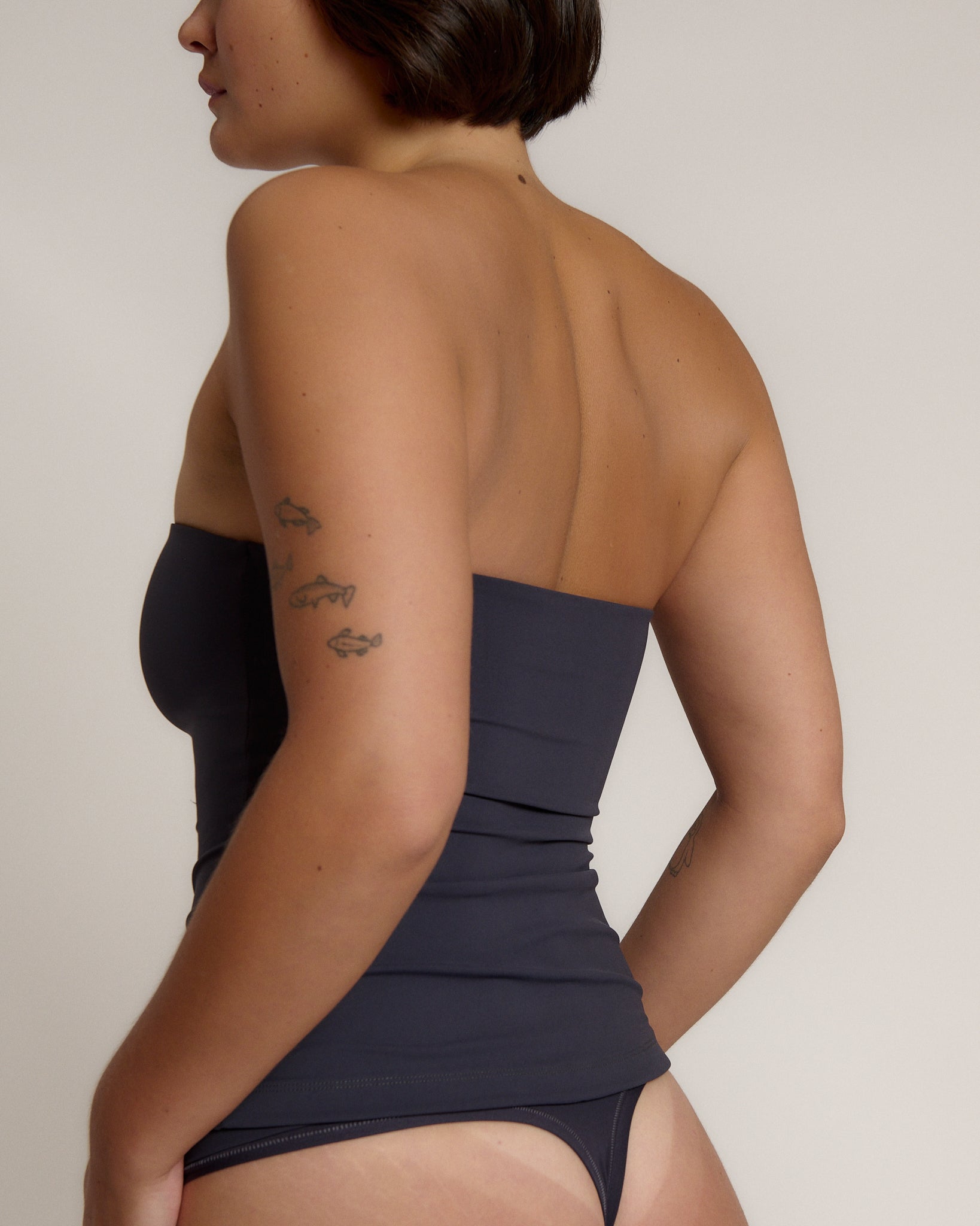 A woman modeling a myst tube top and a matching thong against a plain light gray studio background.