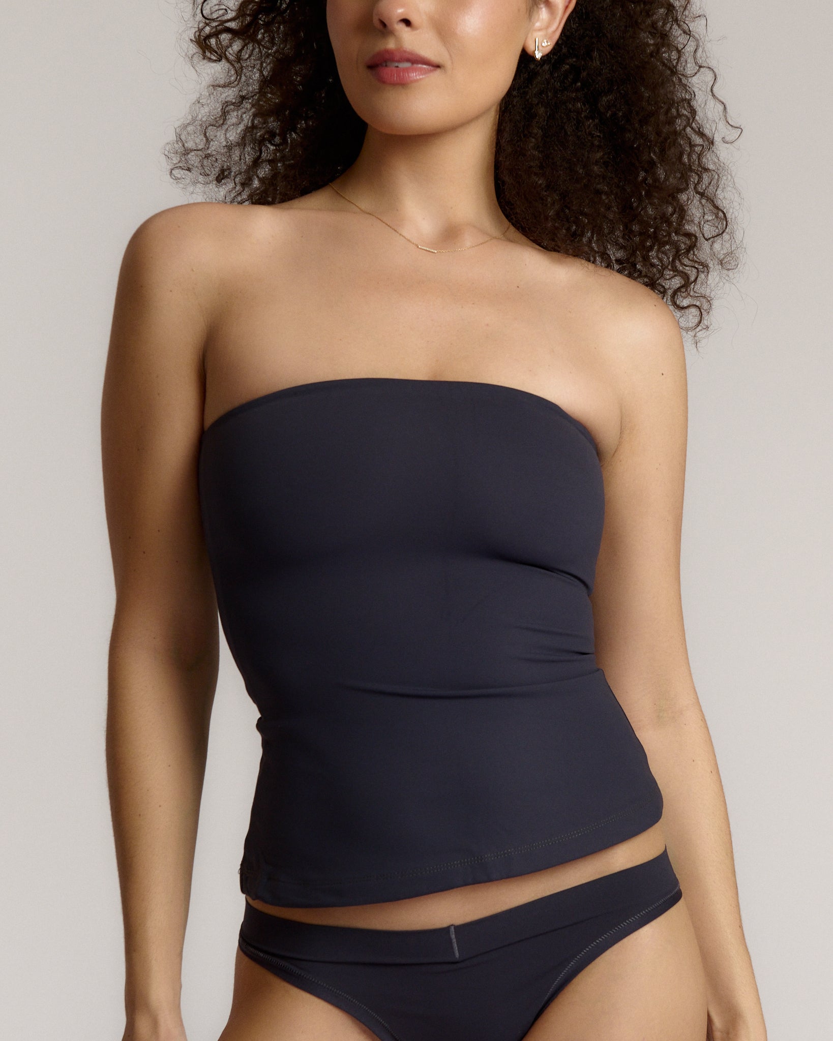 A woman modeling a myst tube top and a matching thong against a plain light gray studio background.