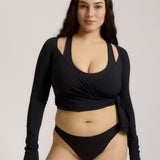 Woman wearing a black wrap top and black thong on a plain background