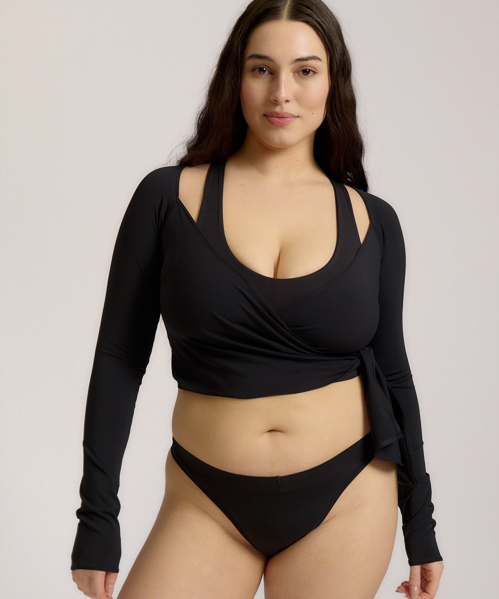 Woman wearing a black wrap top and black thong on a plain background
