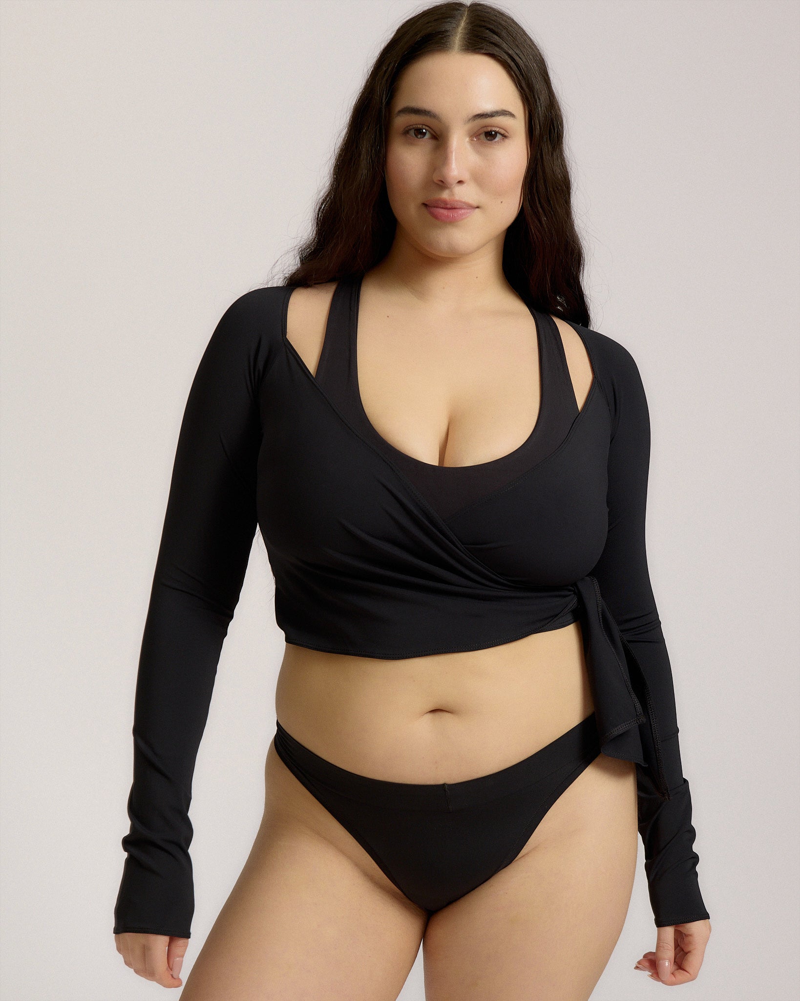 Woman wearing a black wrap top and black thong on a plain background