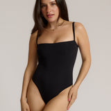 Woman wearing a black bodysuit against a plain background