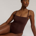 A woman wearing a brown square neck bodysuit with thin straps.