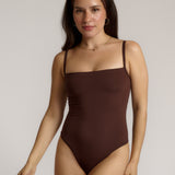 A woman wearing a brown square neck bodysuit with thin straps.